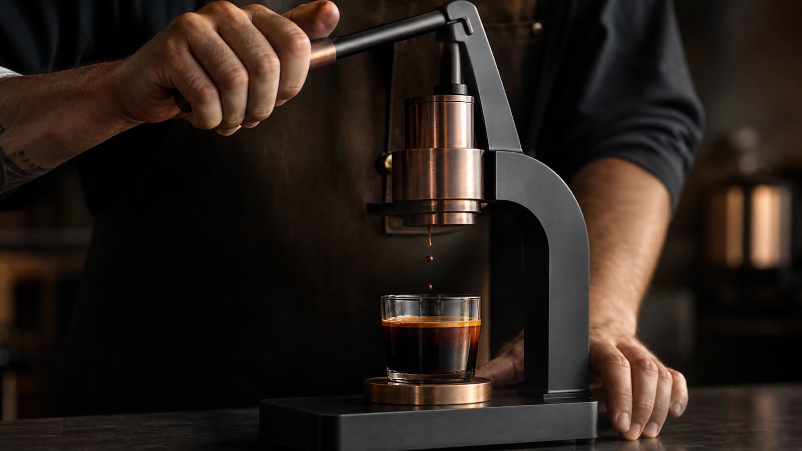 A barista raises the lever on a manual espresso press as the last drops fall into a nearly full clear glass.